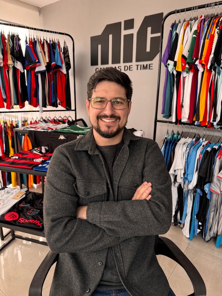 Fundador da MIC Camisas de Time na loja, com araras de camisas ao fundo